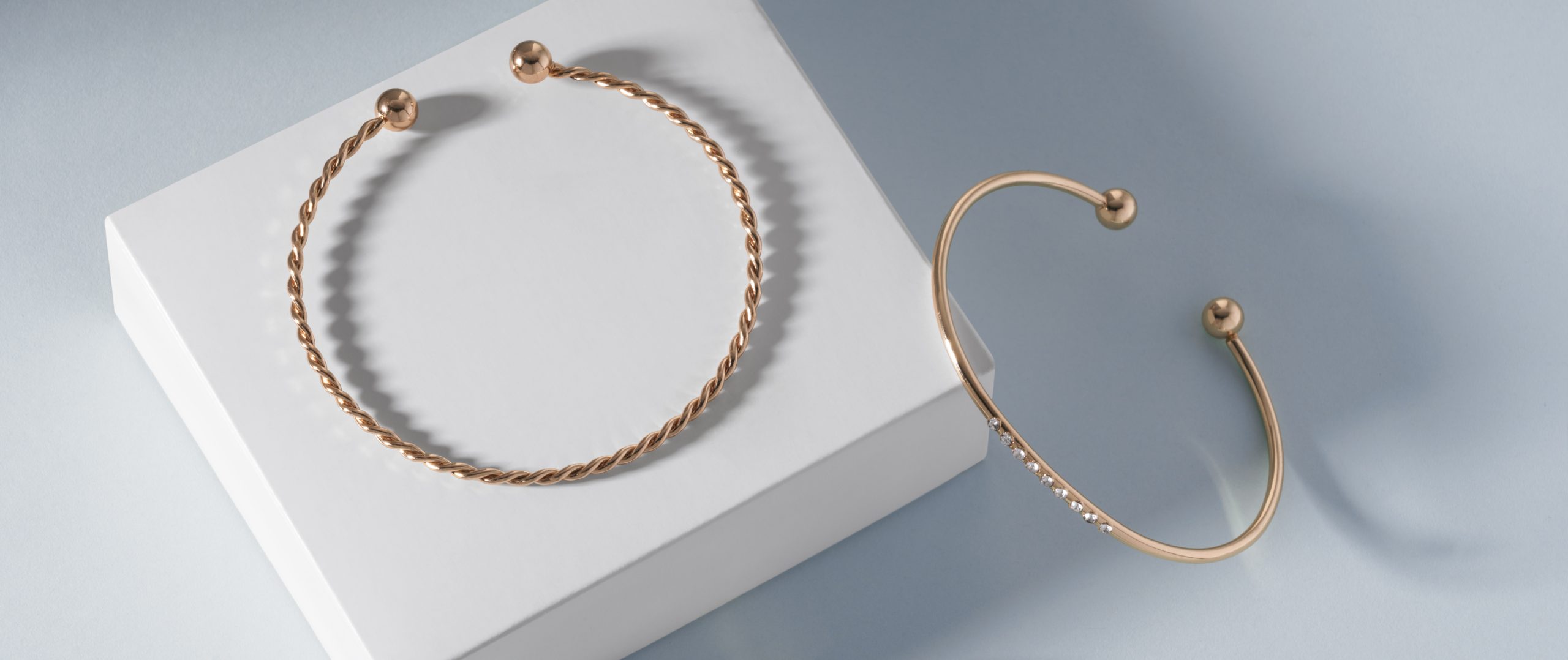 panoramic shot two modern golden bracelets white box blue background with copy space scaled